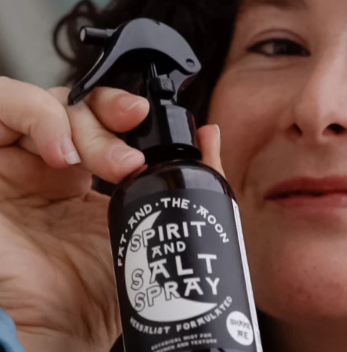 Person holding a bottle labeled 'Spirit and Salt Spray' with a woman in the background.