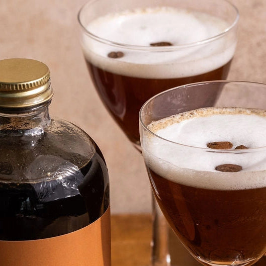 Bottle of Espresso Martini with two glasses on a wooden table.