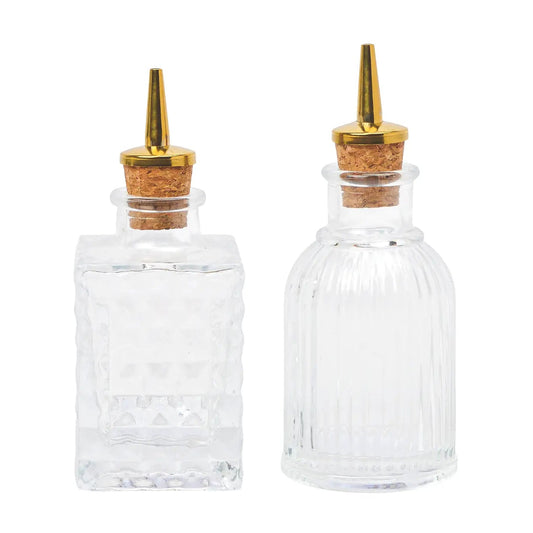 Two clear glass bottles with gold nozzles and cork stoppers on a white background