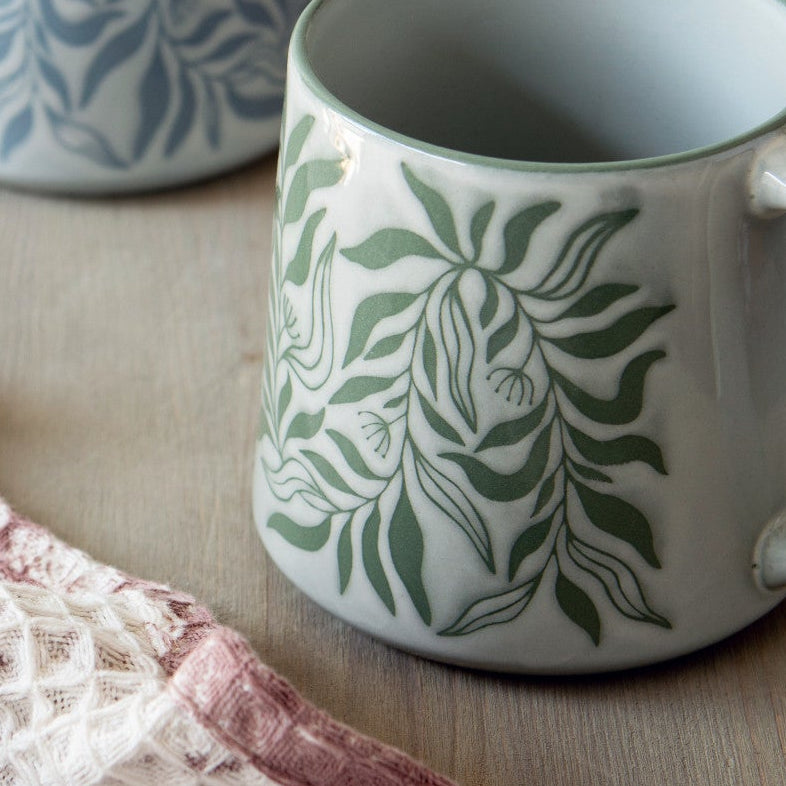 Four patterned mugs on a wooden surface with a lace cloth.