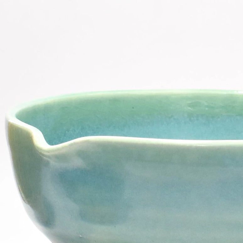 Two ceramic items, a small cup and a larger bowl, with a whisk on a white background.