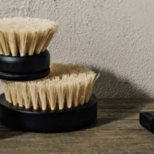 Set of dish brushes with sisal bristles on a wooden surface against a neutral wall.