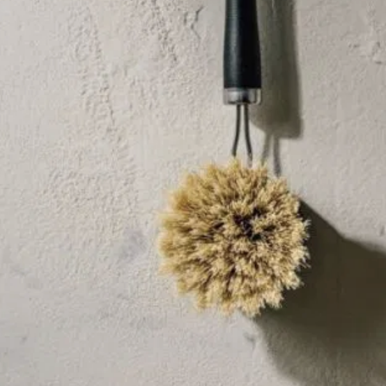 Set of three cleaning brushes with natural bristles hanging on a textured wall.