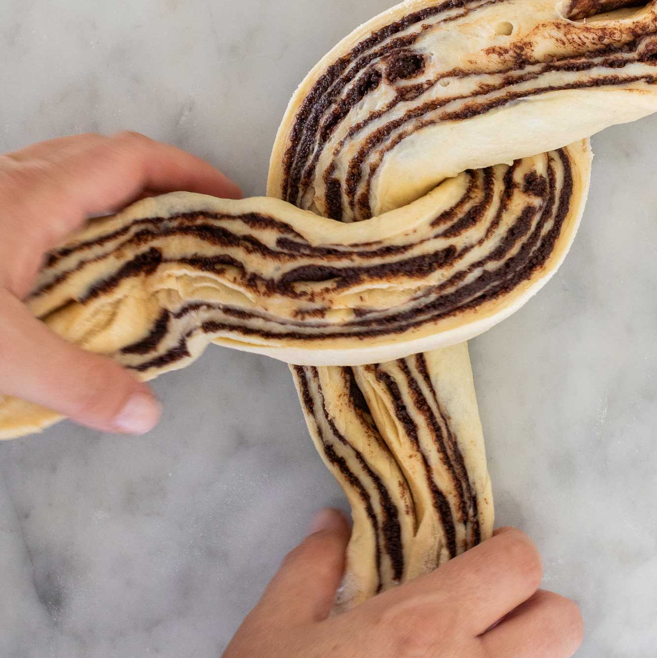 Braided bread with chocolate swirls held by hands on a marble surface