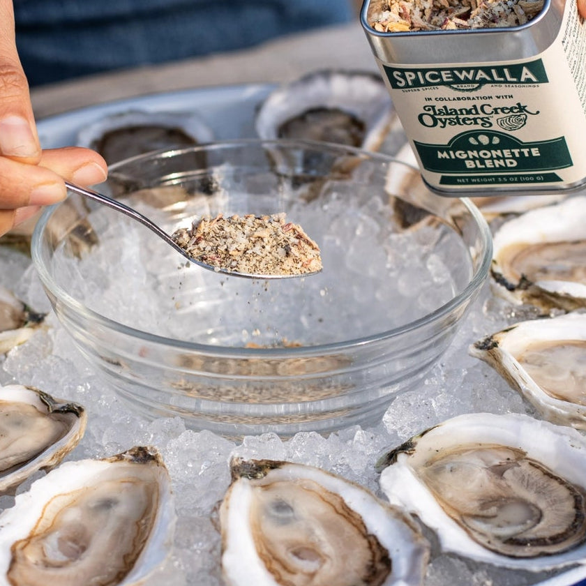 Person seasoning oysters on a half shell with a container of spice.