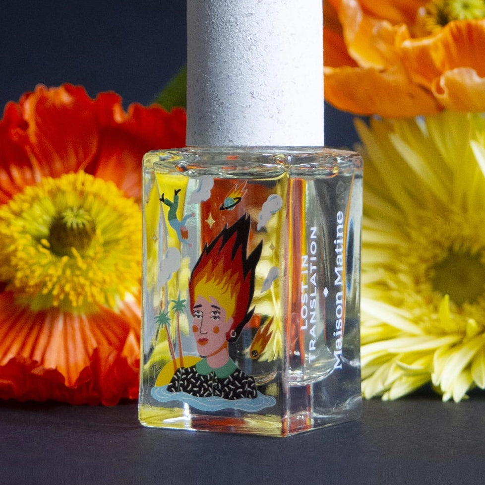 Small bottle with a label featuring a face, surrounded by colorful flowers on a dark background