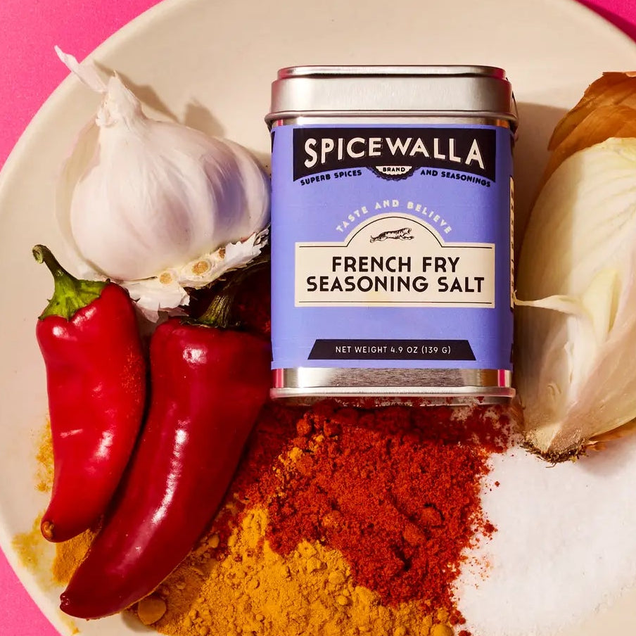 Spicewalla French Fry Seasoning Salt can on a plate with spices and vegetables against a pink background